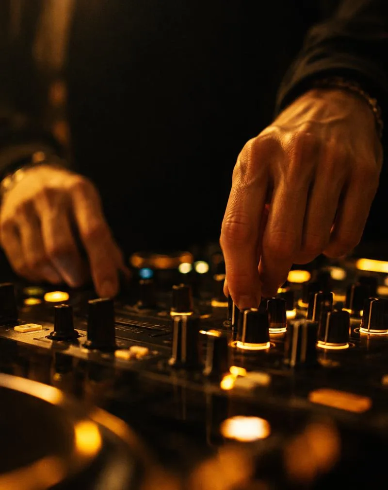 Close-up of DJ hands adjusting glowing mixer controls