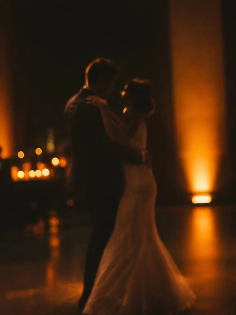 Bride and groom sharing a first dance in warm amber uplighting
