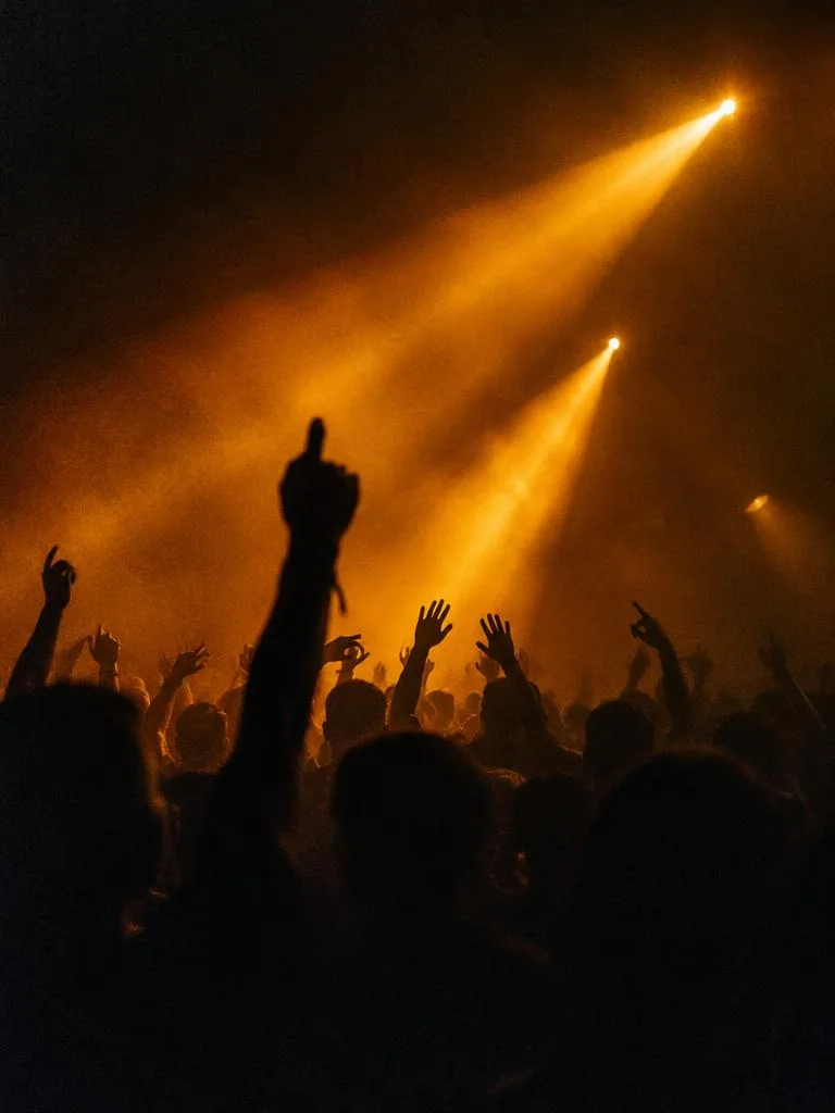 Club crowd with raised hands under amber spotlight beams